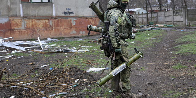 An armed serviceman of Donetsk People's Republic militia walks past a building damaged during fighting in Mariupol on Wednesday.