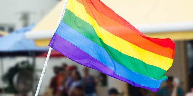  Rainbow flag waving on the street during a gay pride celebration with unrecognizable people lining the sidewalk in the background. U.S. embassies can now display the flag on the same pole as the American flag in June, during Pride month.  