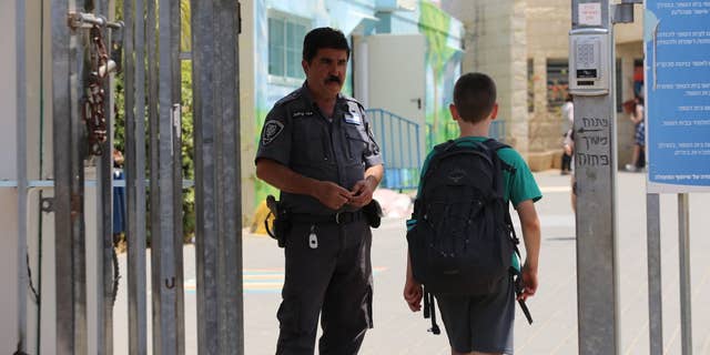 An Israeli school security officer watches on as students enter school 