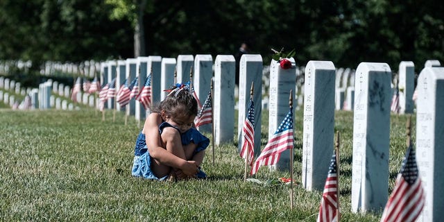 A girl reacts in front of a headstone during Memorial Day as visitors honor veterans and those lost in war at Arlington National Cemetery