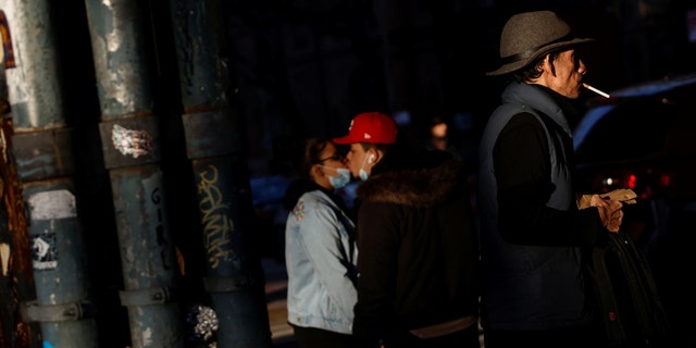 A man walks along a street corner smoking a cigarette while a couple kisses in the Brooklyn borough of New York City, U.S., February 10, 2022. 