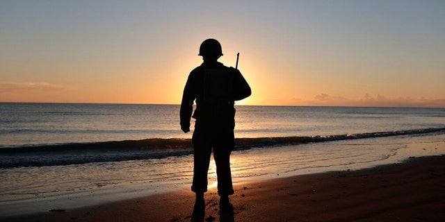 A World War II reenactor pays tribute to soldiers during a D-Day commemoration ceremony of the 78th anniversary for those who helped end World War II, in Saint-Laurent-sur-Mer, Normandy, France, Monday, June 6, 2022. 