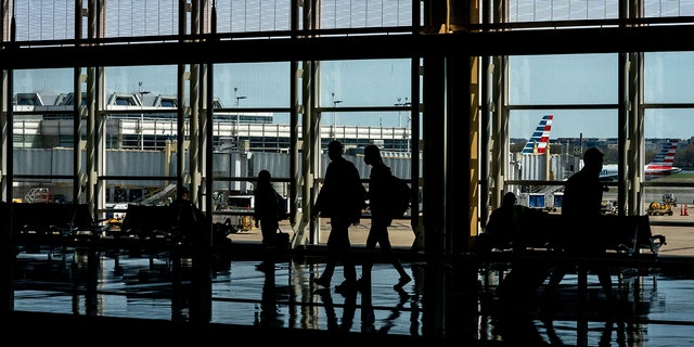 American Airlines aircrafts are seen in the background behind travelers passing through Ronald Reagan Washington National Airport in Arlington, Virginia on April 11, 2022. 