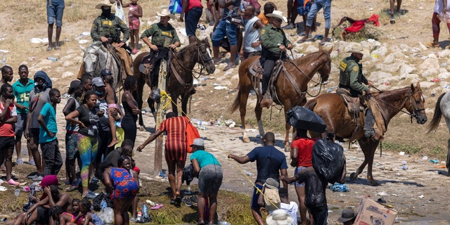 Mounted U.S. Border Patrol agents watch Haitian immigrants on the bank of the Rio Grande in Del Rio, Texas on September 20, 2021, as seen from Ciudad Acuna, Mexico.