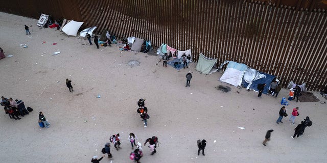 Immigrants gather along the U.S. border wall after crossing through a gap from Mexico Dec. 10, 2021 in Yuma, Ariz. 