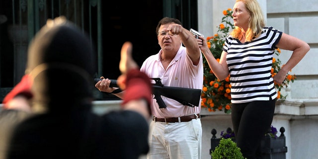 Armed homeowners Mark and Patricia McCloskey stand in front their house as they confront protesters marching to St. Louis Mayor Lyda Krewson's house on June 28, 2020.