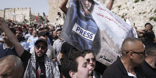 Mourners hold a banner depicting slain Al Jazeera veteran journalist Shireen Abu Akleh as they walk from the Old City of Jerusalem to her burial site, Friday, May 13, 2022. Abu Akleh, a Palestinian-American reporter who covered the Middle East conflict for more than 25 years, was shot dead Wednesday during an Israeli military raid in the West Bank town of Jenin.(AP Photo/Ariel Schalit)