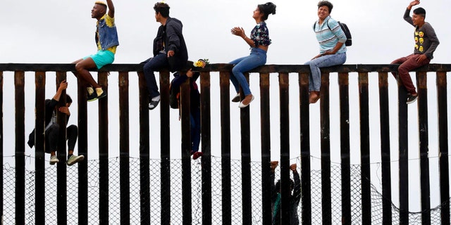 Central American migrants sit on top of the border wall on the beach in San Diego during a gathering of migrants living on both sides of the border, Sunday, April 29, 2018.