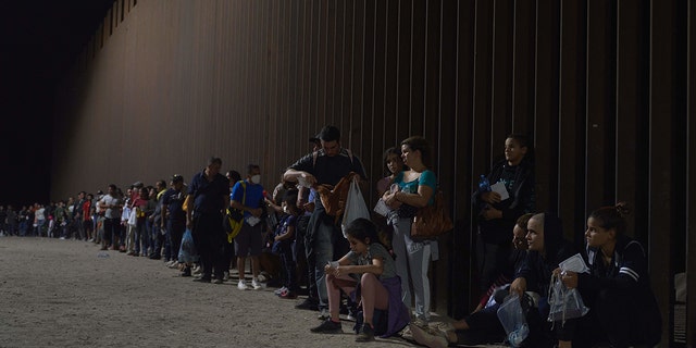 Migrants line up as they wait to be processed by US Border Patrol after illegally crossing the US-Mexico border in Yuma, Arizona in the early morning of July 11, 2022. - 