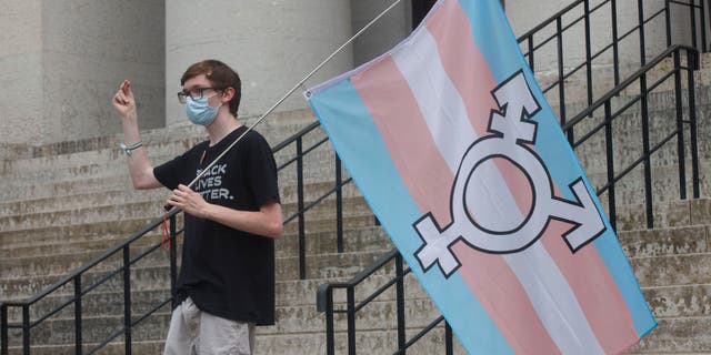 A protester holds the trans flag and snaps in solidarity with other speakers, during a demonstration at the Ohio Statehouse in Columbus, Ohio, on June 25, 2021.