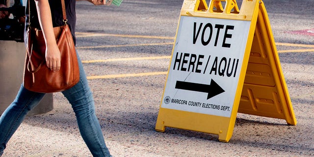 A resident walks past a "Vote Here" sign outside a polling location at the Burton Barr Central Library in Phoenix, Arizona.