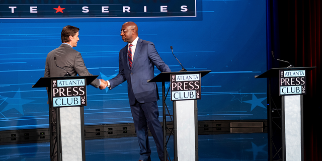 Libertarian challenger Chase Oliver, left, and U.S. Sen. Raphael Warnock, D-Ga., shake hands following the Atlanta Press Club Loudermilk-Young Debate Series in Atlanta, for the U.S. Senate race, Sunday, Oct. 16, 2022. The empty podium at right was for Republican challenger Herschel Walker, who was invited but did not attend.