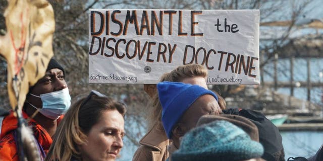 A man holds a sign reading "Dismantle the Discovery Doctrine" as people march during the National Day of Mourning on Thanksgiving Day, Nov. 25, 2021, in Plymouth, Massachusetts.