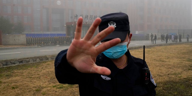 A security person moves journalists away from the Wuhan Institute of Virology.