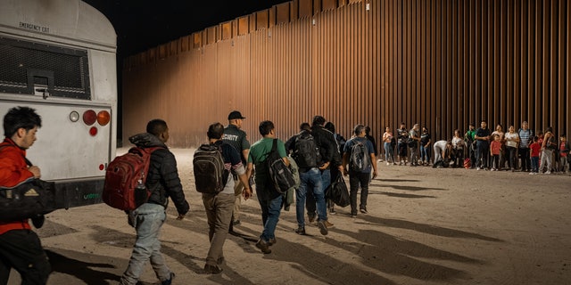 Immigrants wait to be processed by the U.S. Border Patrol after crossing the border from Mexico, with the U.S.-Mexico border barrier in the background, on Aug. 6, 2022 in Yuma, Arizona. 