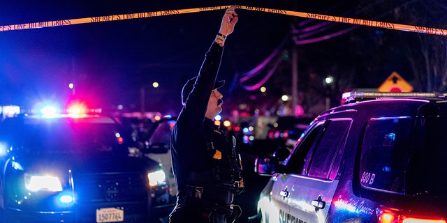 A sheriff's deputy in California holds up police tape to allow a vehicle to enter a crime scene.