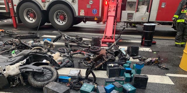 Several e-bikes and lithium-ion batteries are seen strewn on the street as New York City firefighters fight a nearby fire.