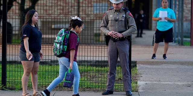 Students with their backpacks walk into school, passing a police officer in uniform