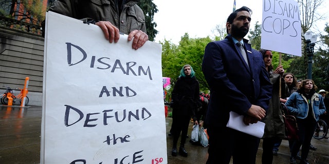 Protesters hold signs reading "disarm cops" and "defund the police" in Portland, Oregon