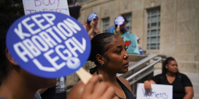 Pro-choice advocates stand outside with signs, one sign saying "Keep Abortion Legal"