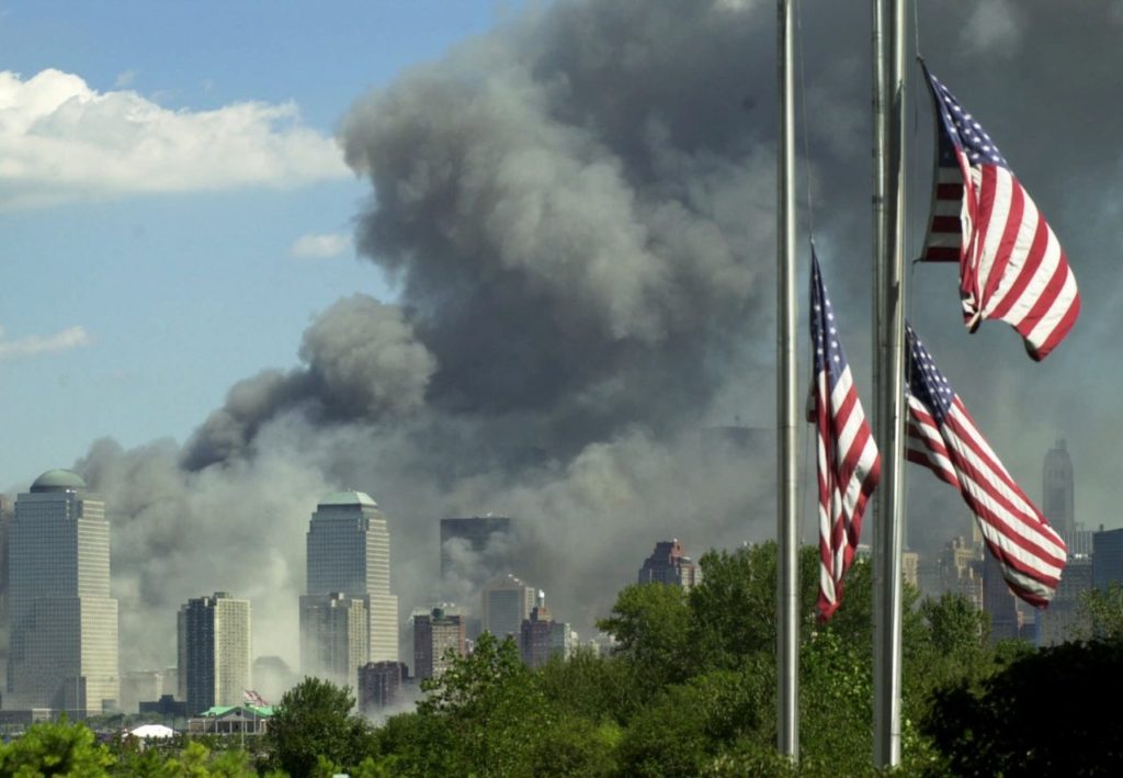 Flags fly at half-staff at the Liberty Science Center in Jersey City, N.J. as a large cloud of smoke billows from a fire at the World Trade Center in New York, Tuesday, Sept. 11, 2001. In one of the most devastating attacks ever against the United States, terrorists crashed two airliners into the World Trade Center in a closely timed series of blows that brought down the twin 110-story towers. (AP Photo/Daniel Hulshizer)