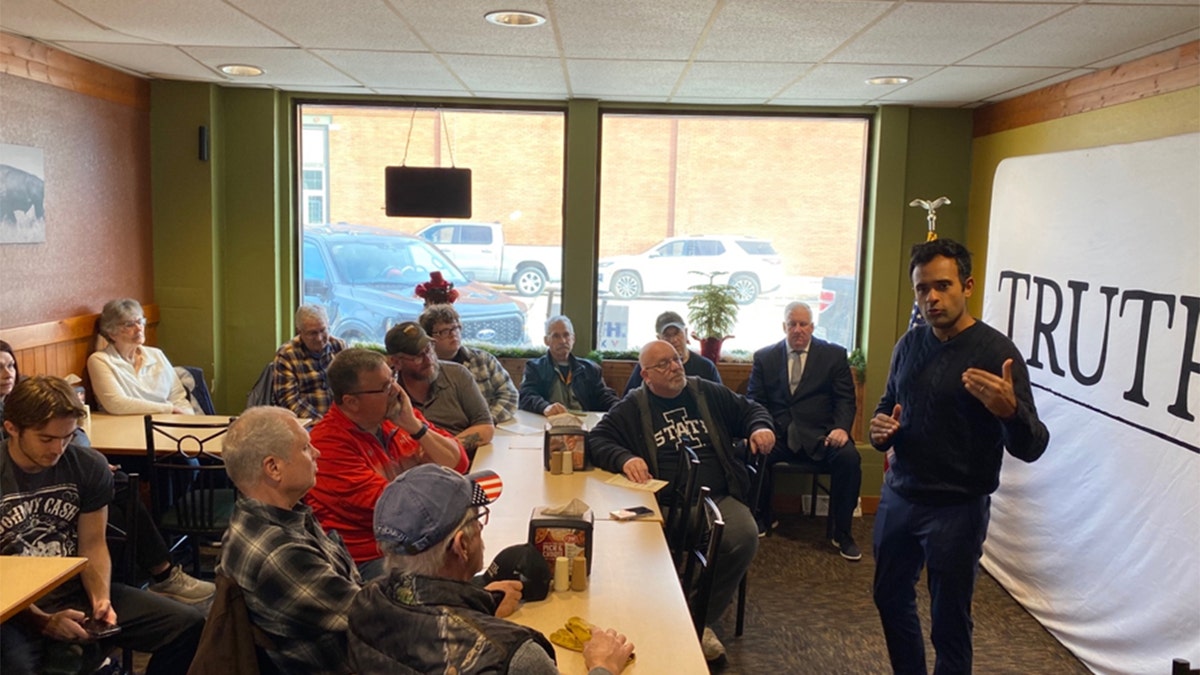 Vivek Ramaswamy speaking into microphone, talking to Iowa voters sitting at/around a table