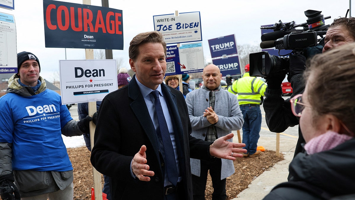 Rep. Dean Phillips speaking to voters, men and women behind him with campaign signs for him, Trump, and Write-In Joe Biden