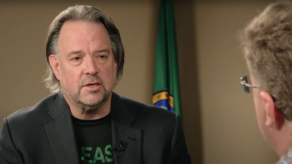 Brian Heywood sits in front of Washington state flag