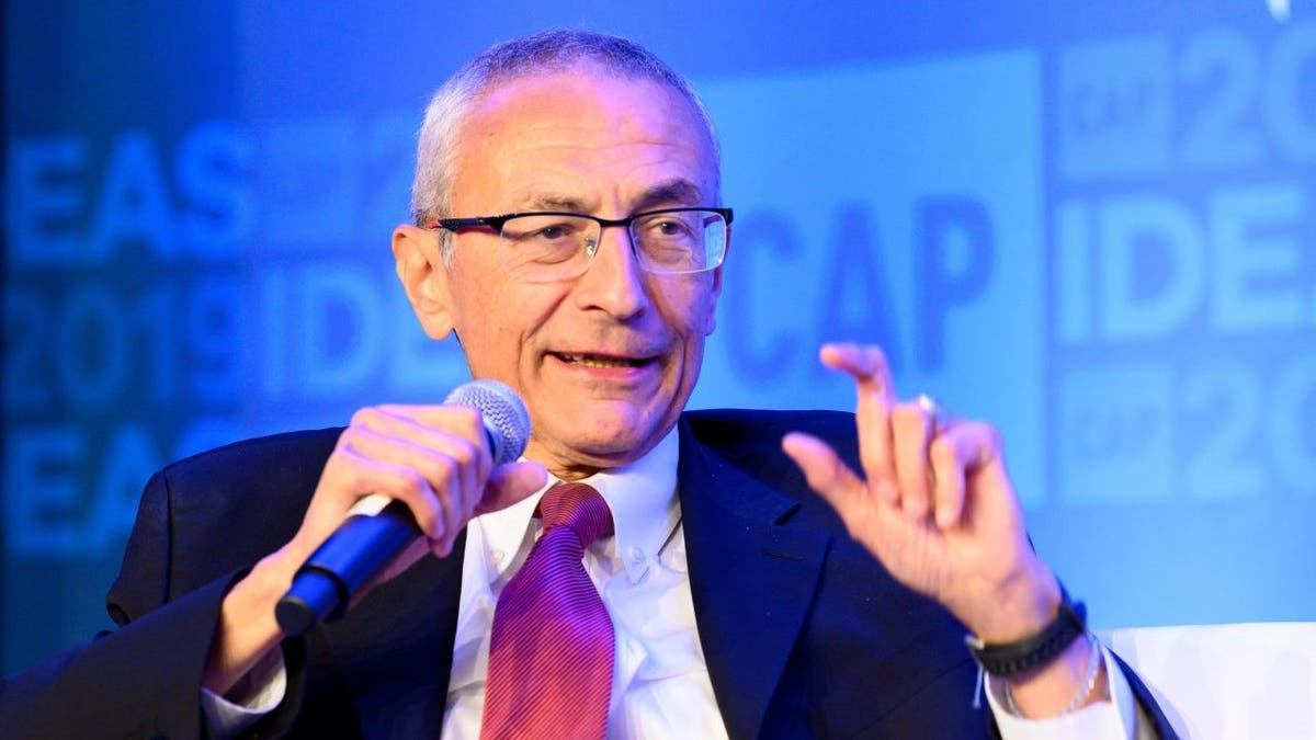 John Podesta seated, speaking into handheld microphone