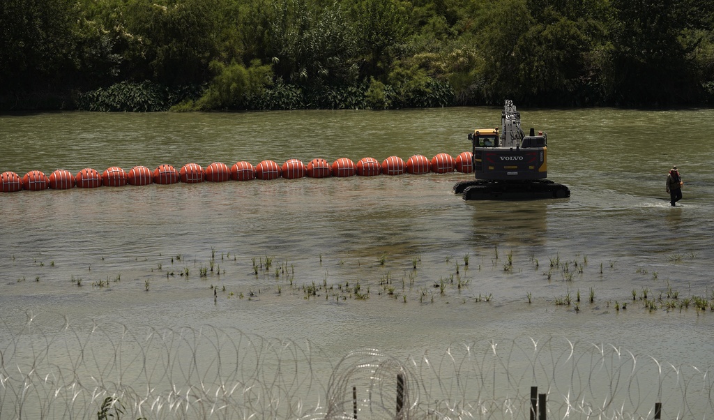 Workers deploy a string of large buoys to be used as a border barrier at the center of the Rio Grande.