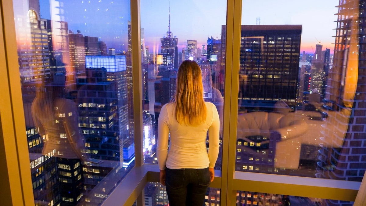 Woman looking out highrise apartment window to city outside