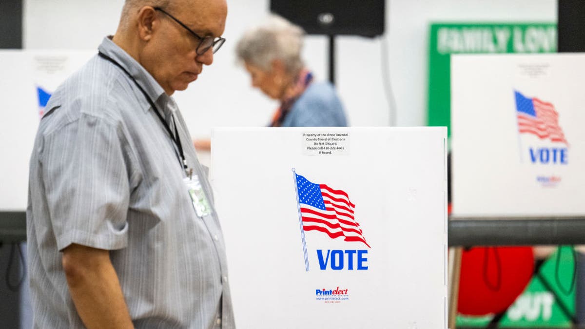 Maryland Board of Elections poll workers pass by empty booths during the Maryland state primary election at a polling station in Annapolis, Maryland, on May 14, 2024.