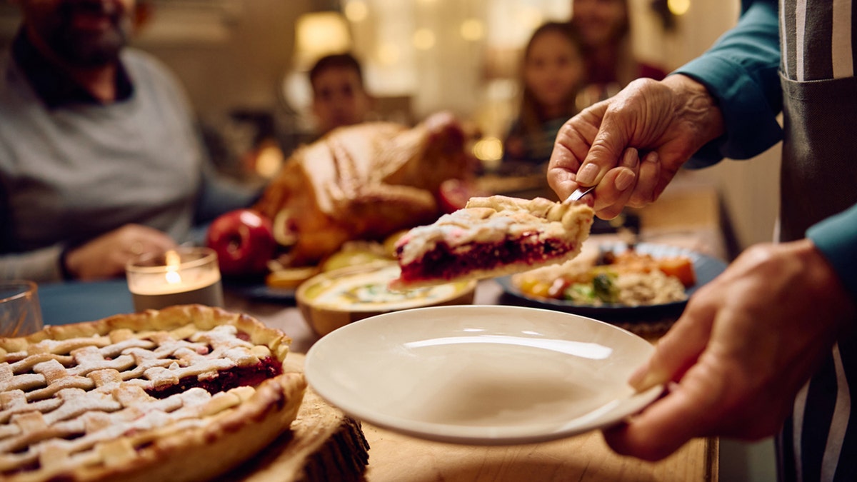 family member serving Thanksgiving pie to her family at dining table.