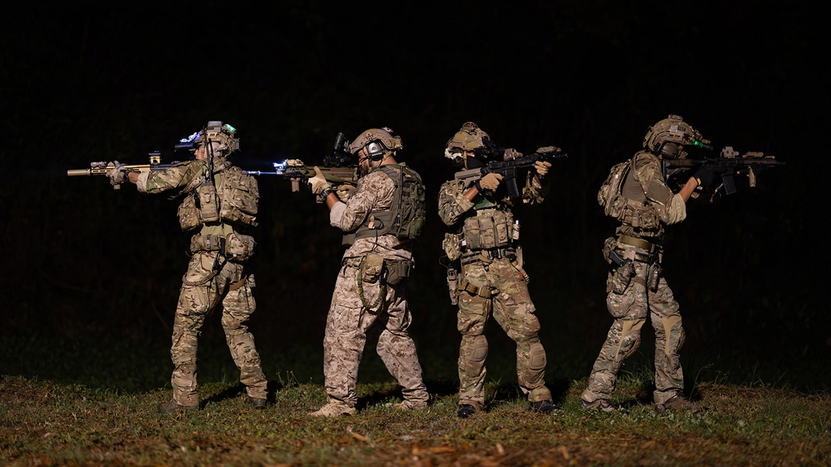 Soldiers in camouflage uniforms aiming their rifles ready to fire during military night operation