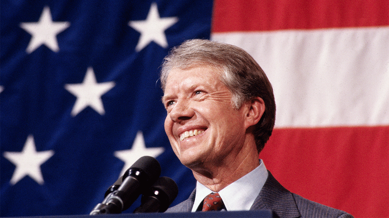 Jimmy Carter smiling in closeup shot, US flag behind him