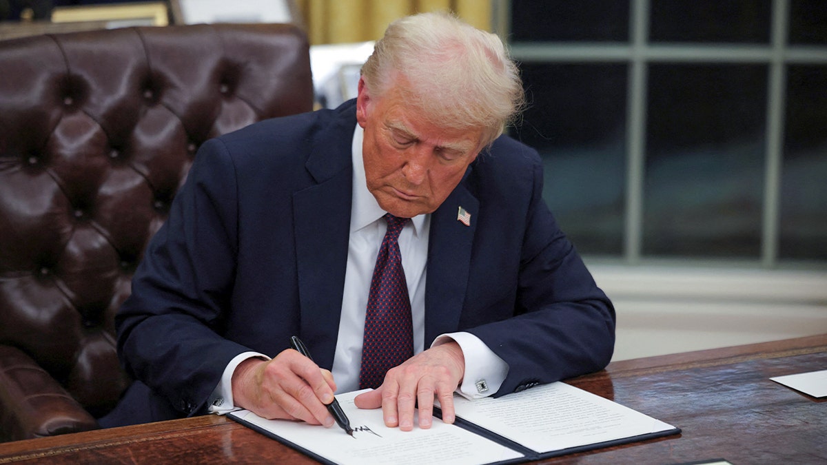 Trump at Oval Office desk signing document