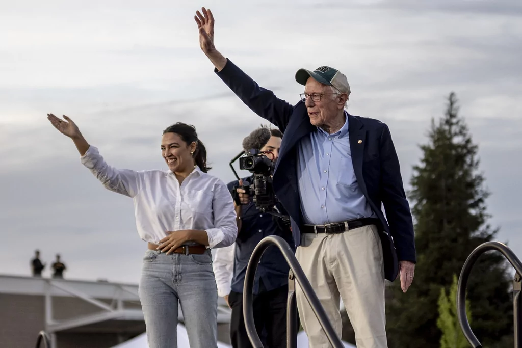 Rep. Alexandria Ocasio-Cortez (D-NY), left, and Sen. Bernie Sanders (I-VT) wave during a stop of the 'Fighting Oligarchy' rally at Folsom Lake College in Folsom, Calif., Tuesday, April 15, 2025. 