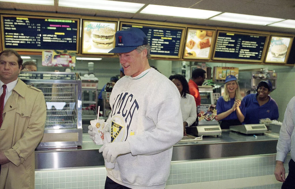 With a cup of coffee and a cold drink in his hands, President-elect Bill Clinton leaves a local McDonald's restaurant in downtown Little Rock, Arkansas, Jan. 13, 1993. The fast-food establishment is one of Clinton's usual stops during his morning jogs. (AP Photo/Greg Gibson)