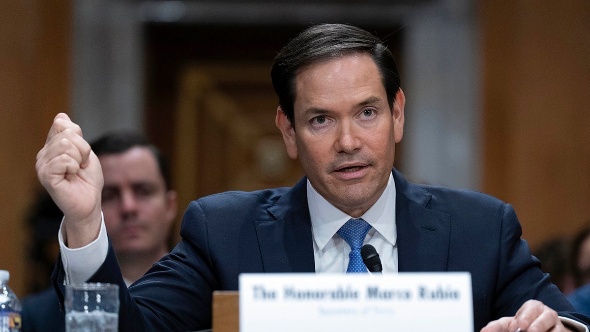 Secretary of State Marco Rubio testifying in a dark suit and blue tie