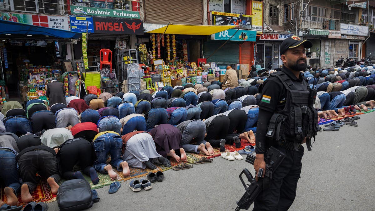 Kashmiri Muslims offering Friday prayers while Indian security guard stands watch