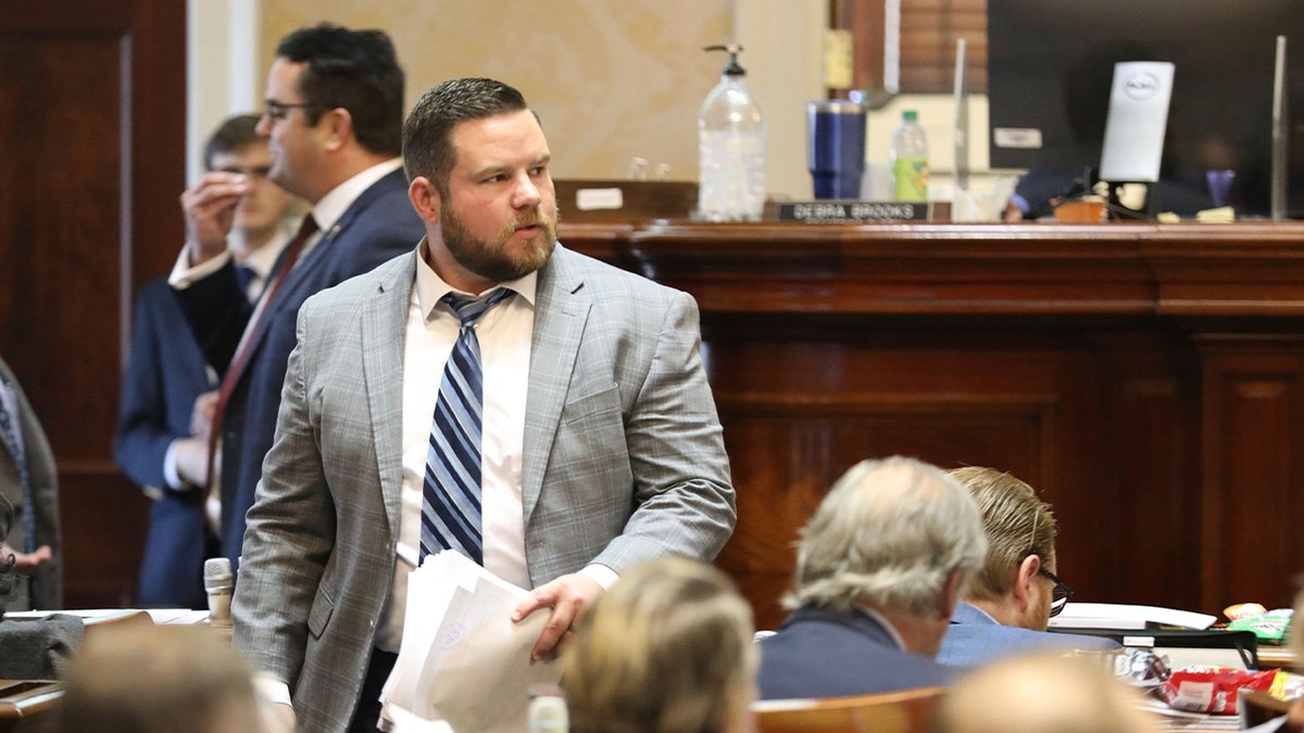 Robert John May III, wearing a grey suit, walks down the aisle of the House