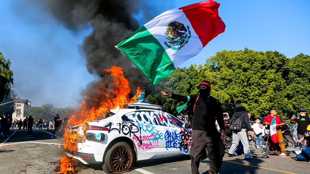 car on fire as masked protester waves Mexican flag