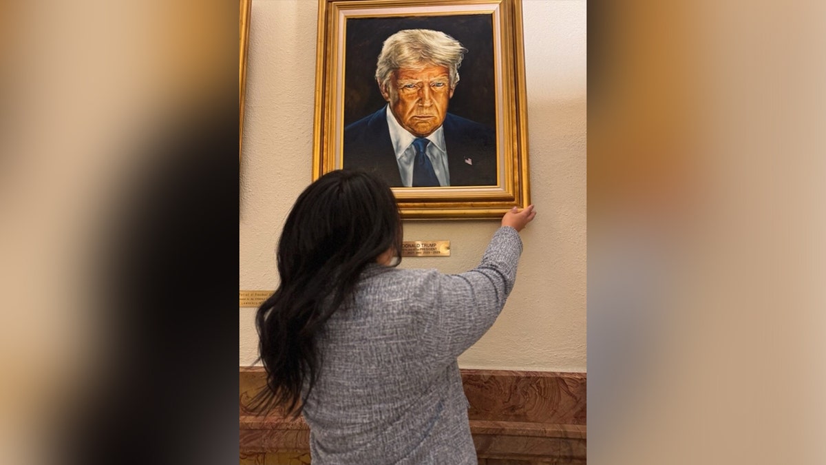 woman hangs new trump portrait of the president looking serious