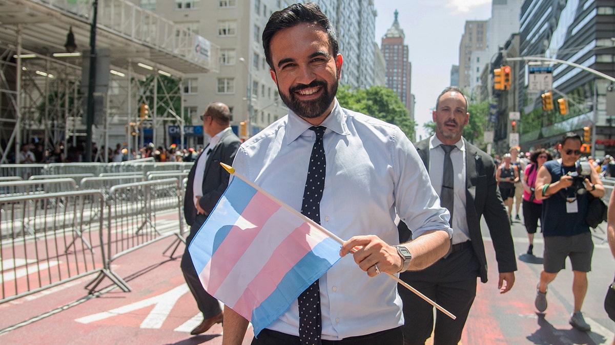 Zohran Mamdani holding transgender pride flag, smiling