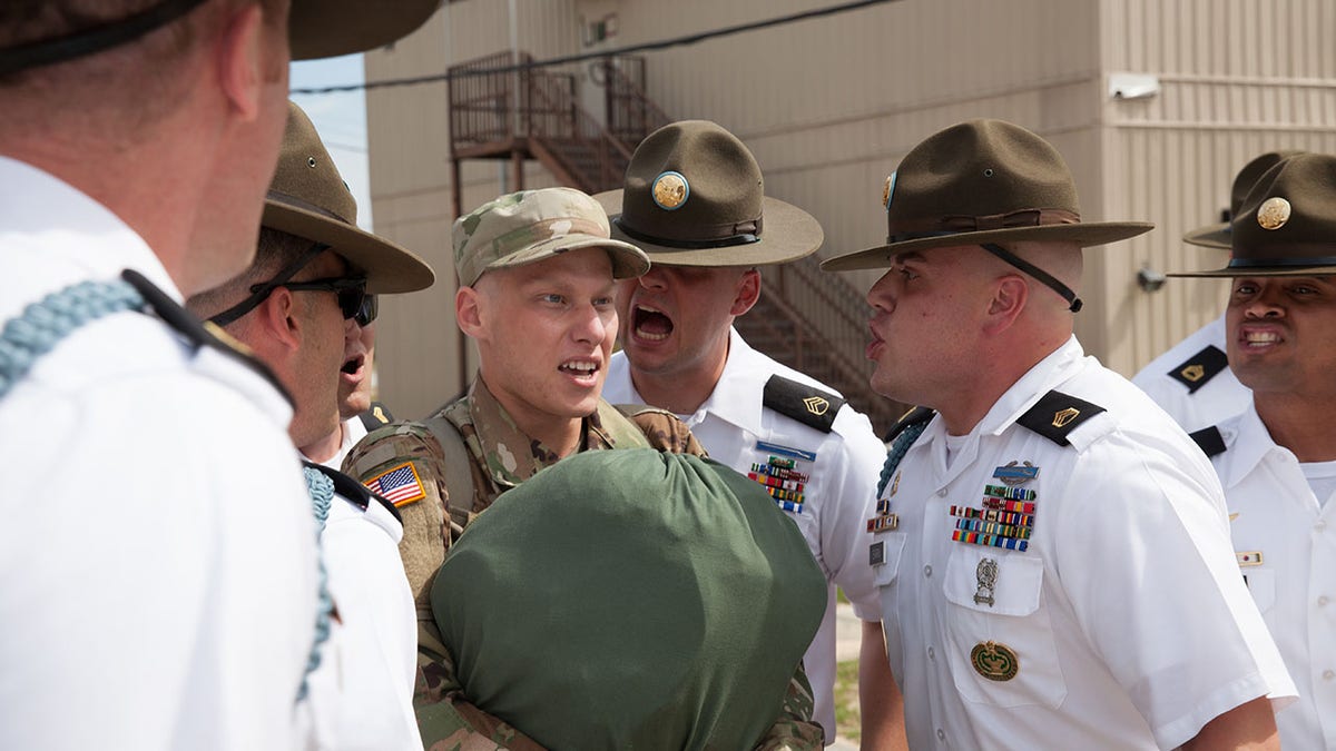 Army drill sergeants screaming at a trainee in basic training.