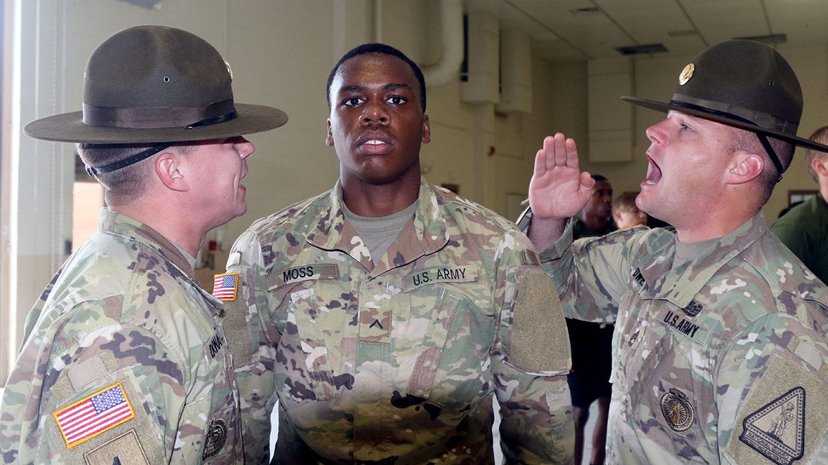 A U.S. Army solider stands while drill sergeants take turns yelling at him.