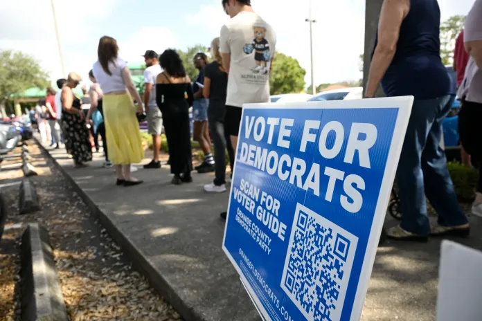 A Vote For Democrats sign is viewed as people stand in line to vote in the general election outside of an early voting location, Wednesday, Oct. 30, 2024, in Orlando, Fla. 