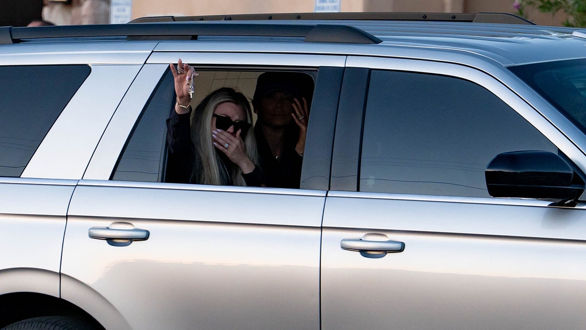 Erika Kirk holding a cross out of a vehicle window.