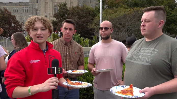 four students standing with pizza