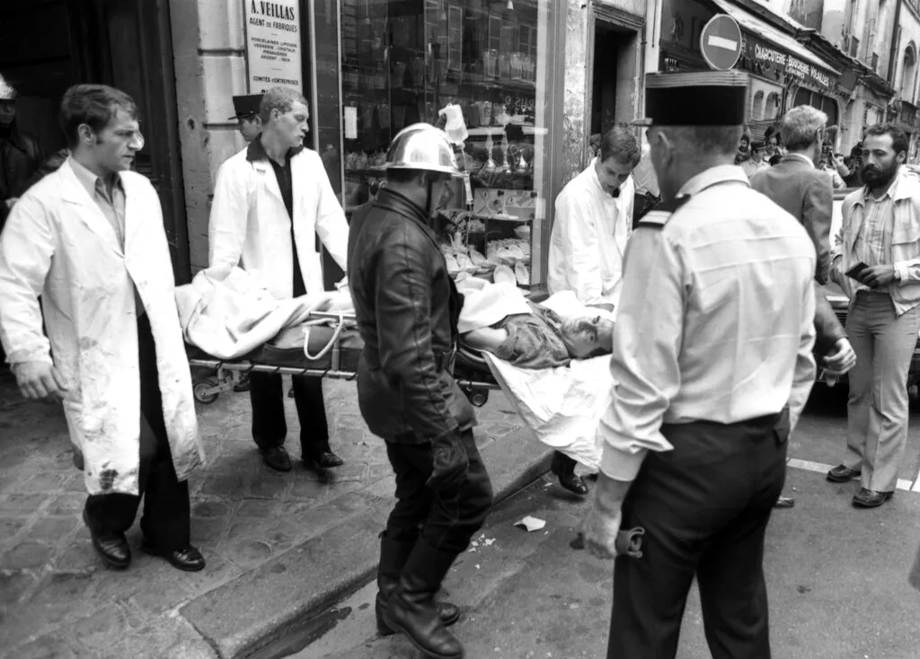 This Aug. 9, 1982, file photo shows a police officer looking at an injured man being carried away on a stretcher from the scene of a terror attack at Jewish restaurant and deli Jo Goldenberg in Paris, France. The suspected mastermind of an attack on a Paris Jewish restaurant in 1982 that left six people dead and 22 injured has been arrested in Jordan, a source close to the case said Wednesday June 17, 2015. 